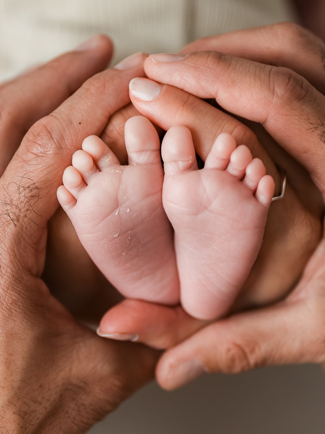 Los pies de un bebé recién nacido sostenidos entre las manos de dos adultos